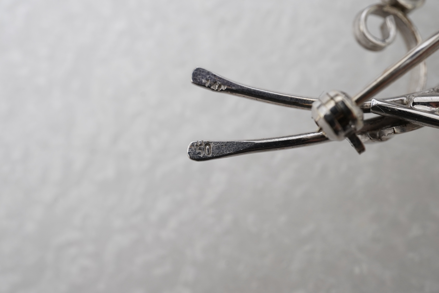 A diamond brooch, designed as stylised foliate spray in white gold, accented with three brilliant-cut diamonds totalling approximately 0.15 carats, length 5.2cm, stamped 750, gross weight 5 grams.